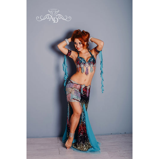Woman in a multicolor sequin belly dance costume with fringe, open sides, and turquoise chiffon panels